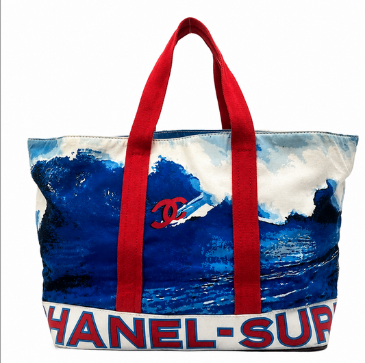 A Chanel tote bag featuring a blue ocean wave print, red fabric handles, and a white bottom band with 'CHANEL-SUP' text in red and blue.