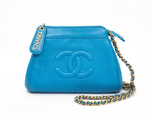 A Chanel shoulder bag in bright blue pebbled leather with an embossed interlocking CC logo, a gold-tone chain strap, and a blue leather tag with gold lettering, shown on a white background.