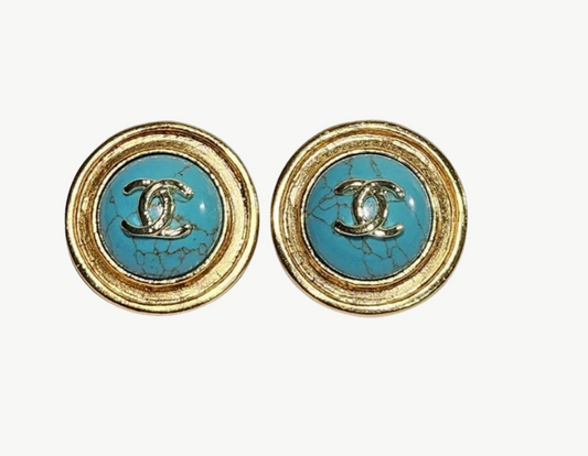 A pair of Chanel round stud earrings featuring a light blue turquoise center with a gold-tone interlocking CC logo and a textured gold-tone bezel, set against a plain light background.
